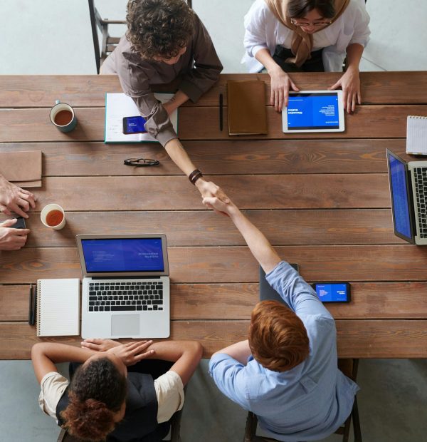 Overhead view of colleagues in a work meeting using laptops and tablets, emphasizing teamwork and technology.
